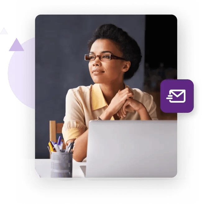 Woman at her desk holding her smartphone with a laptop in the background