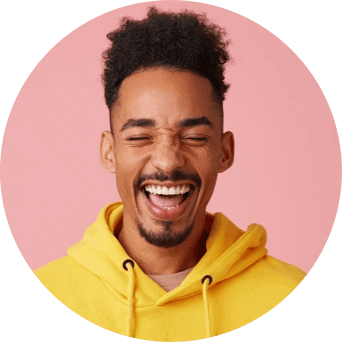 A man wearing a yellow hooded sweatshirt smiles wide while closing his eyes.